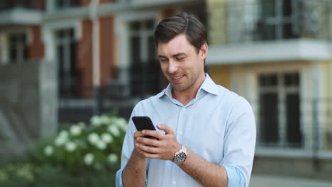 Happy-man-typing-on-phone-outdoors