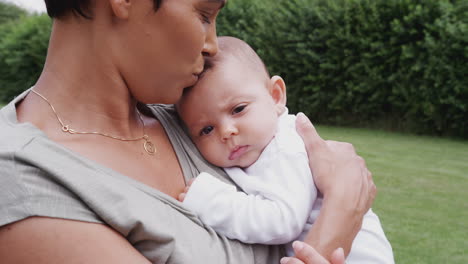 loving mother holding and kissing 3 month old baby daughter in garden at home