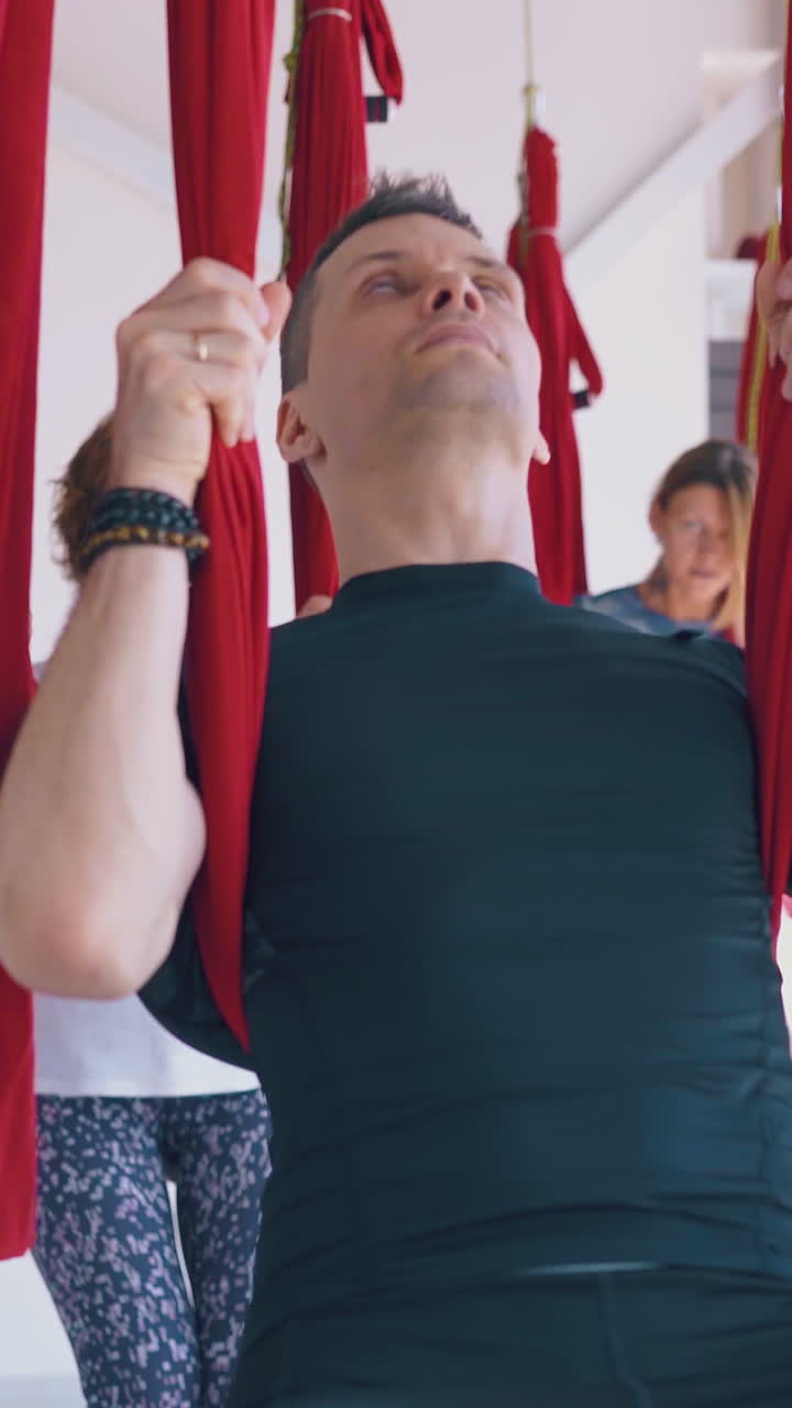 sporty gentleman with ladies relaxes leaning on special red hammocks after advanced fly yoga class close view