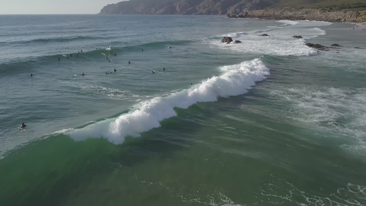 antena, reversa, toma de drones de surfistas esperando olas, uno montando una ola, en una tarde soleada, cascais, portugal