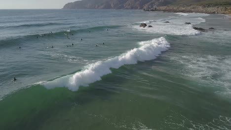 aerial, reverse, drone shot of surfers waiting for waves,one riding a wave, on a sunny evening, cascais, portugal