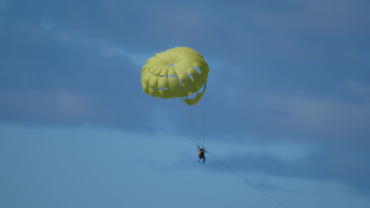 una pareja haciendo parasailing desciende colgada de un paracaídas amarillento
