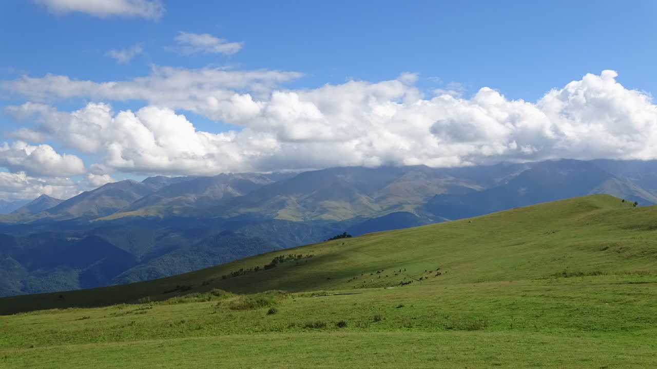 Filmato in timelapse di nuvole in movimento e luce mutevole su un prato alpino verde e una lontana catena montuosa del Caucaso in Russia, ampia vista panoramica.