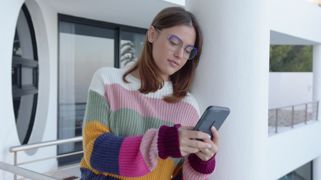 Texting on smartphone, young woman in colorful sweater standing outdoors