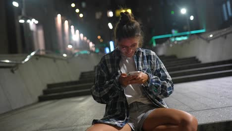 young woman using smartphone on city stairs at night