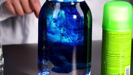 Observe the mesmerizing swirl of blue liquid in a jar beside a green can.