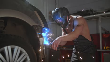 welder sexy mechanic dancing naked doing sparks on a car metal body, in a mask with big muscular biceps, 50 fps ready for slow motion