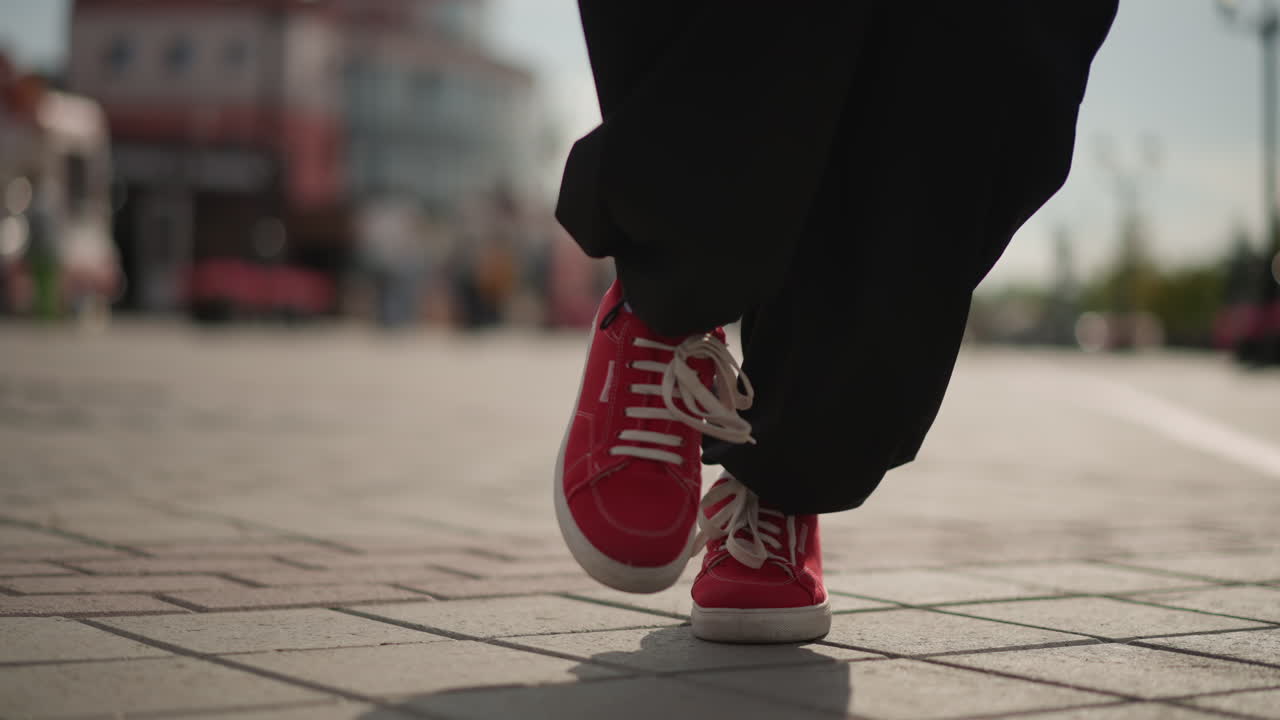 Kırmızı spor ayakkabıların kaldırıma teması, şehirli sokak dansçısı, belirtilmemiş ırk, güneşli plazada ritmik adımlar atan bağcıklı ayakkabıların düşük açılı yakın çekimi, bulanık şehir arka planı, günlük siyah pantolon