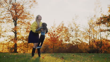 The-mother-plays-with-the-child,-tosses-and-catches-it.-At-sunset-in-a-beautiful-autumn-park