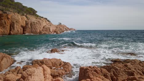 Olas-Del-Océano-Rompiendo-En-El-Bosque-Mediterráneo-De-Acantilados-Terrosos-En-Cami-De-Ronda-España-Costa-Brava,-Paisaje-Rocoso,-Mar-Azul-Rompiendo