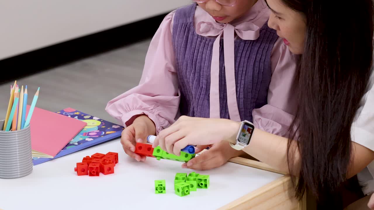 Teacher guides young student connecting colored counting cubes at classroom table with steady close-up camera