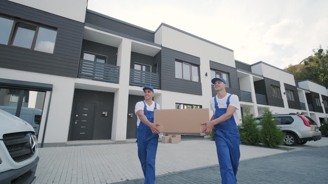 Two young workers of removal company are loading boxes and furniture into a minibus