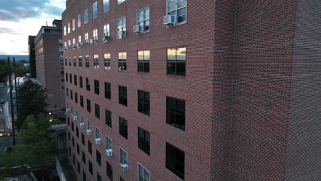 brick apartment building at dusk, reflecting windows, tree shadows on facade, clear sky