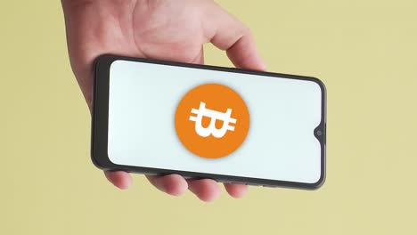 vertikale nahaufnahme einer männlichen hand, die das telefon hochhält und das bitcoin-symbol zeigt