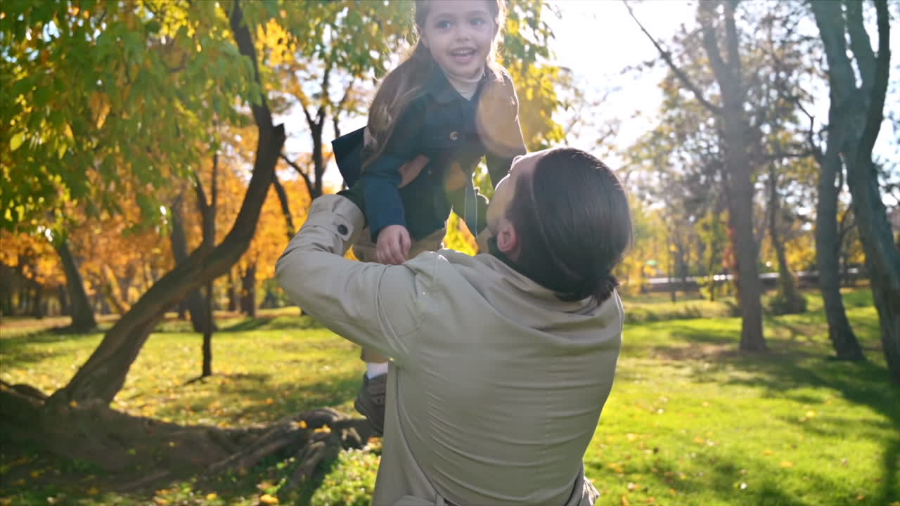 Happy family in an autumn park. Father took his daughter in his arms and kissed her. Slow motion