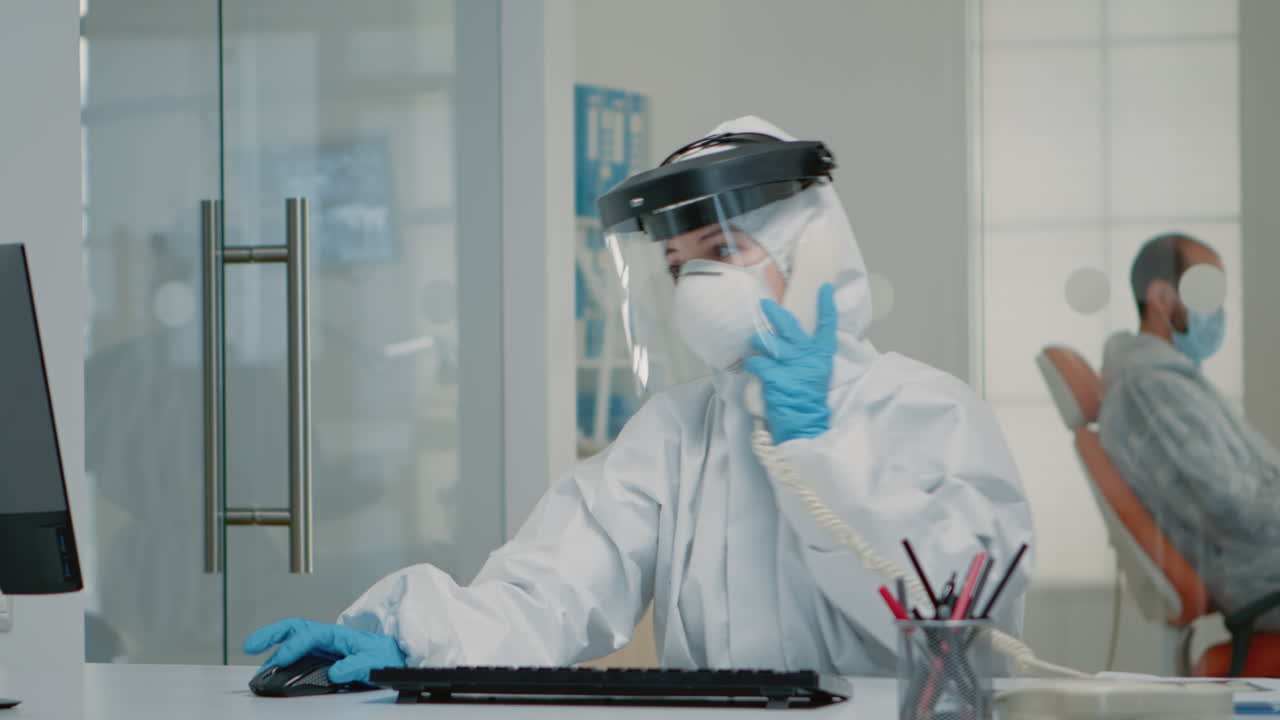 Nurse wearing ppe suit sitting at oral care clinic desk