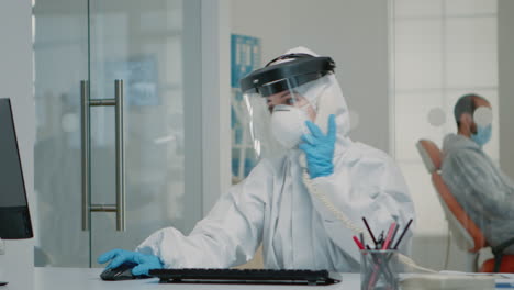 nurse wearing ppe suit sitting at oral care clinic desk