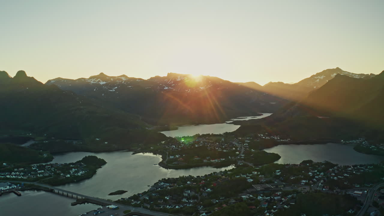 Aerial drone shot over the Norwegian town of Svolvaer in the Lofoten Islands, Norway. Bird's eye view of the fishermen's town at the midnight sun. View of the vast mountains in the background.