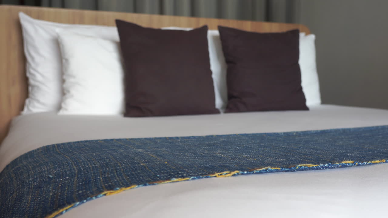imagen inclinada de una cómoda cama de hotel perfectamente hecha con almohadas esponjosas blancas y marrones y un exclusivo edredón de algodón a cuadros sobre una colcha de color blanco puro