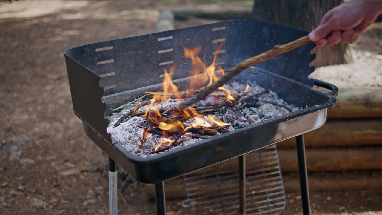 Fire burning bbq grill in park surrounded by trees closeup. Man hand preparing