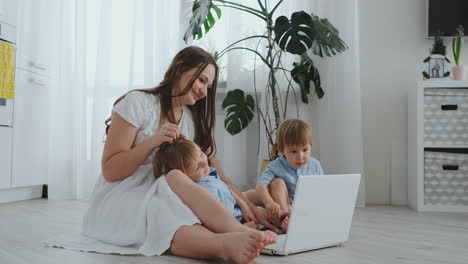 hermosa familia joven moderna acostada en el suelo en casa y haciendo algo en la computadora portátil