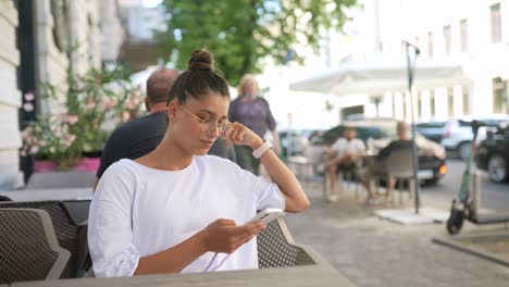 mujer joven usando el teléfono en una cafetería al aire libre