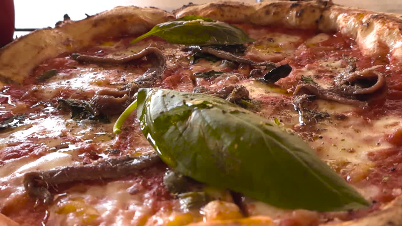 Close up view of anchovy pizza with melted cheese tomato sauce and fresh basil leaves. Traditional pizza filmed in sunlight at a local Portuguese street pizzeria