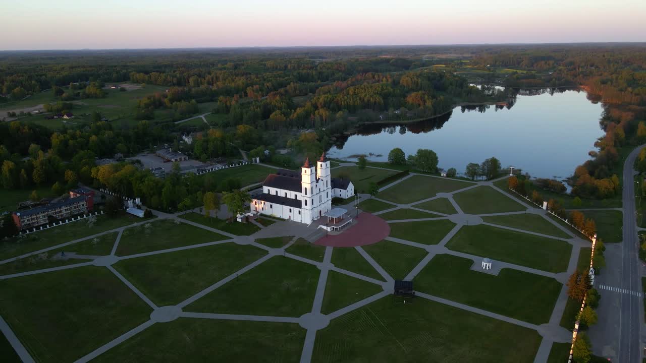 Drone footage circling the Basilica of the Assumption of Blessed Virgin Mary in Aglona Latvia capturing the iconic Baroque-style church its grounds and surrounding serene landscapes at sunset