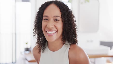 Portrait-of-happy-biracial-woman-with-dark-curly-hair-smiling-at-home,-in-slow-motion