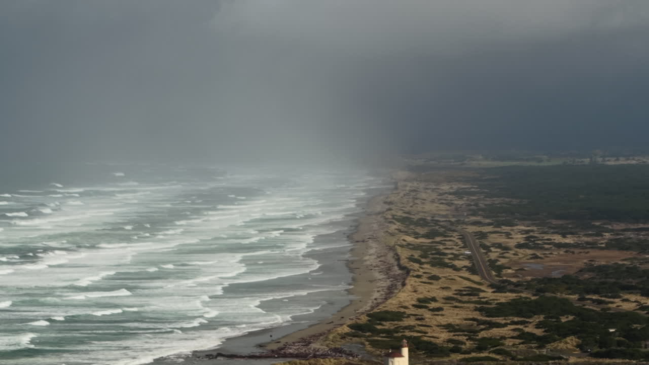 Luftfoto av Oregon Coast Lighthouse i Bandon under stormfullt vær. Tåke- og regnskyer over stranden.