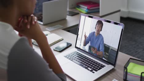 mujer de negocios afroamericana sentada en un escritorio usando una computadora portátil haciendo una videollamada con un colega masculino