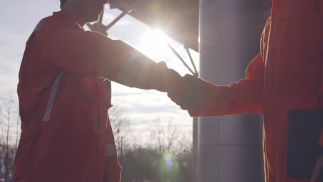 close up view of two construction workers in orange uniform and hardhats shaking hands at the building object