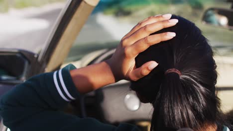 Rear-view-of-woman-driving-along-country-road-in-convertible-car