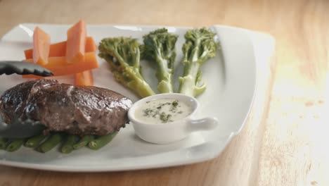toma deslizante de un plato cuadrado con verduras y luego la porción de bistec junto a la olla de salsa encima de las judías verdes dentro de la cocina