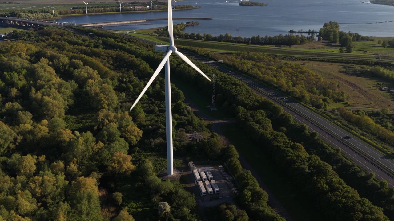 Vista aerea di un sistema di accumulo a batterie accanto a una turbina eolica, che mostra l'accumulo di energia rinnovabile, il supporto alla rete e l'infrastruttura energetica sostenibile.