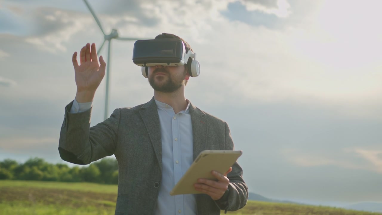 Man wearing virtual reality headset and holding tablet in field with wind turbine background
