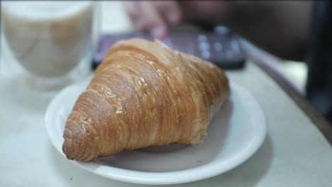cerrar mientras un hombre usa las redes sociales de teléfonos móviles y toma una panadería de croissant francés recién hecho de un plato con enfoque selectivo para el desayuno o la merienda ligera del té de la tarde