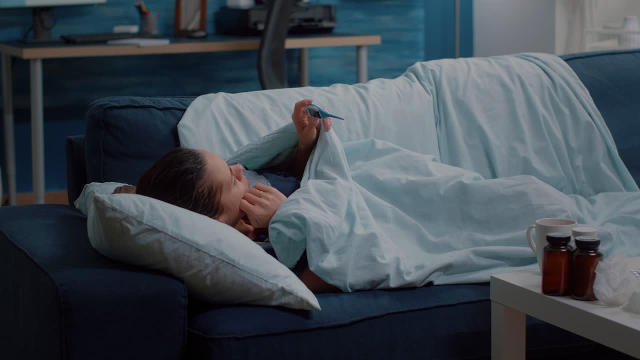 Ill person laying on couch and holding thermometer