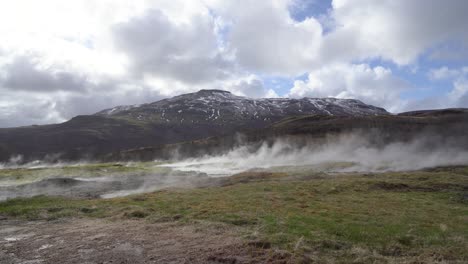 actividad geotérmica en islandia con vapor que se eleva desde el suelo contra un telón de fondo de montañas y un cielo nublado