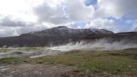 geothermal activity in iceland with steam rising from the ground against a backdrop of mountains and a cloudy sky