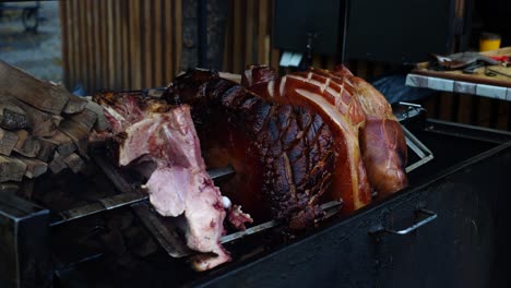 Juicy-beechwood-smoked-ham-rotate-above-grill-on-skewer-near-firewood