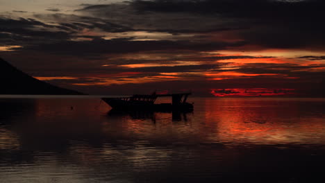 a silhouette of a volcano and small boat during a fiery sky sunset as the camera zooms in to focus on the boat