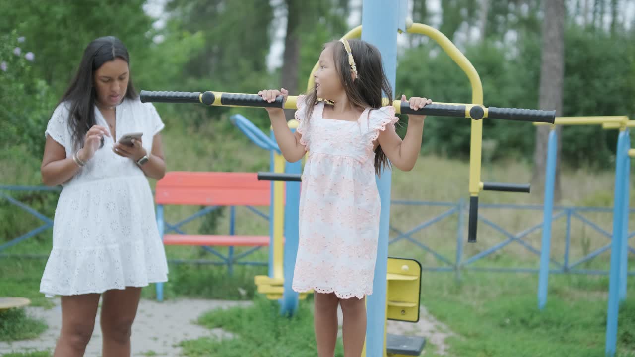 una madre embarazada y su hija joven disfrutan de un tiempo de juego juntos en un patio de recreo en el parque, rodeados de árboles y vegetación