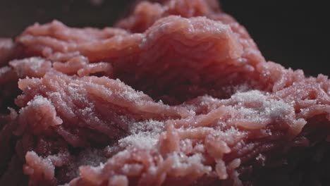 macro shot of ground or minced meat frying in a dark nonstick frying skillet pan with seasoning sprinkled in, preparing as a filling for a tortilla