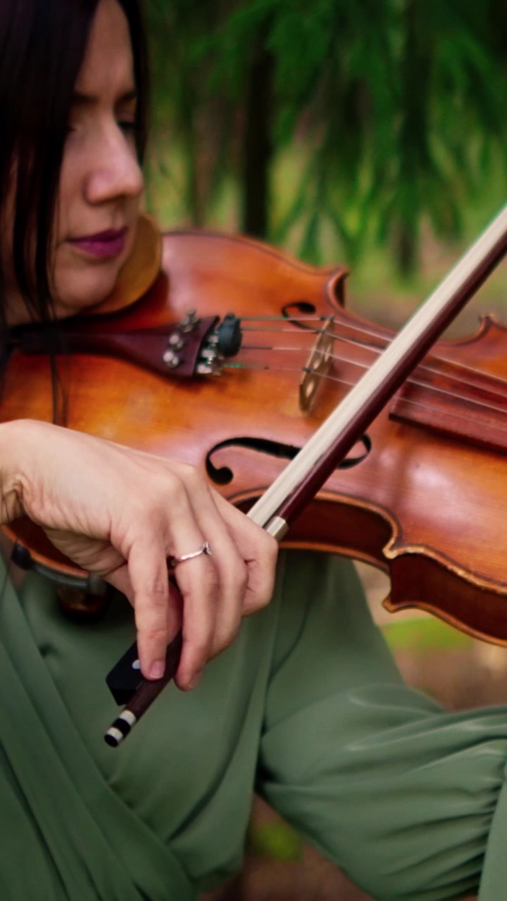Mulher tocando violino em um cenário de floresta.