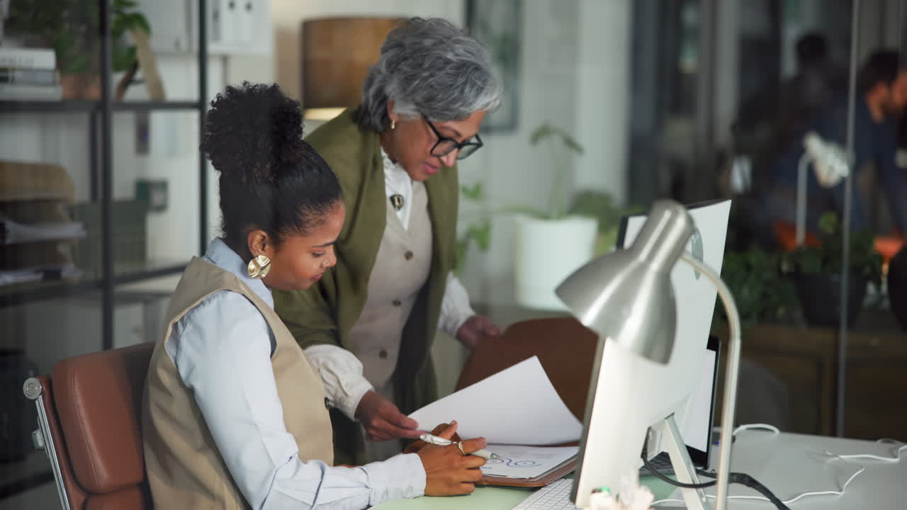 Mature and Young Businesswomen Collaborating on Documents in Office