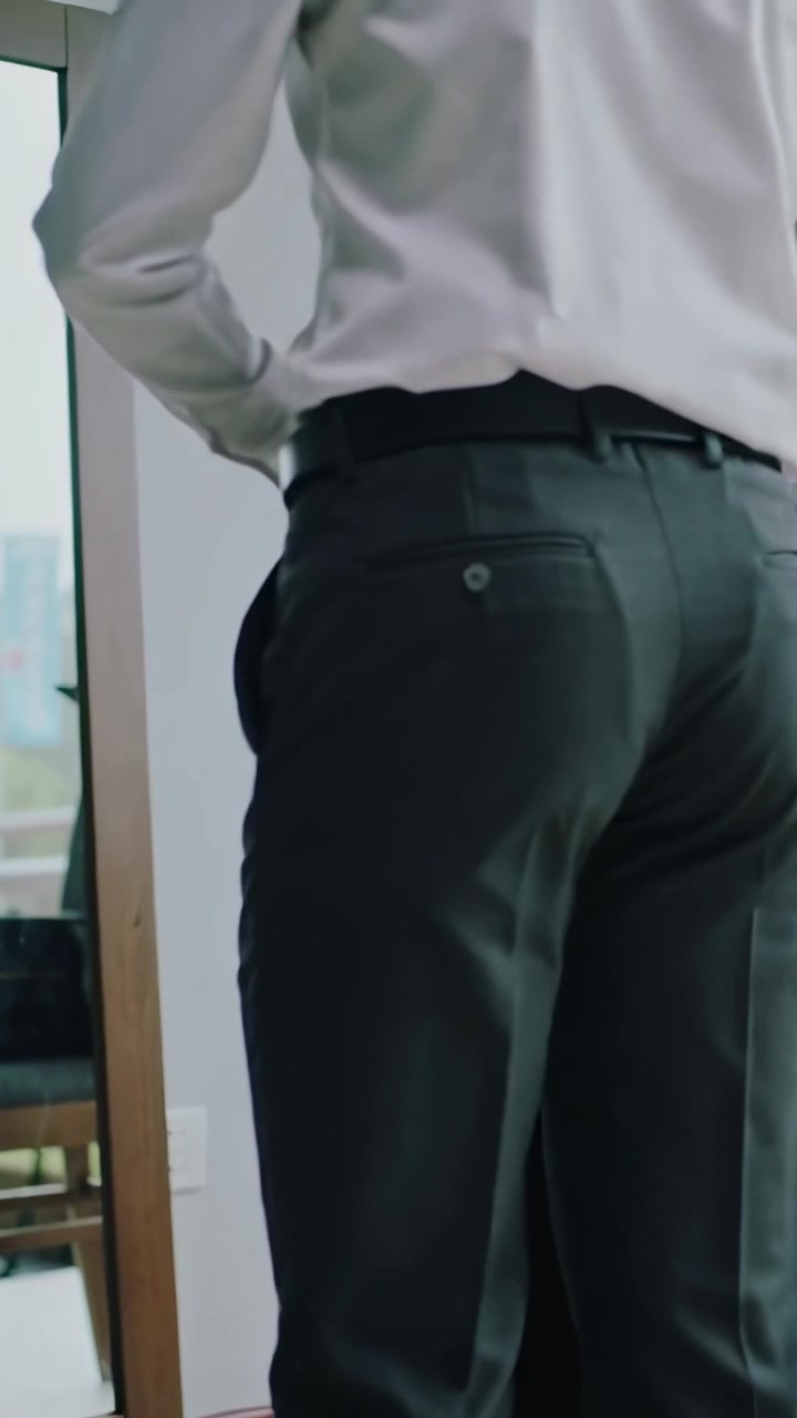 Vertical video: Adjusting man fixing belt, tucking shirt, donning blazer by mirror in room for work