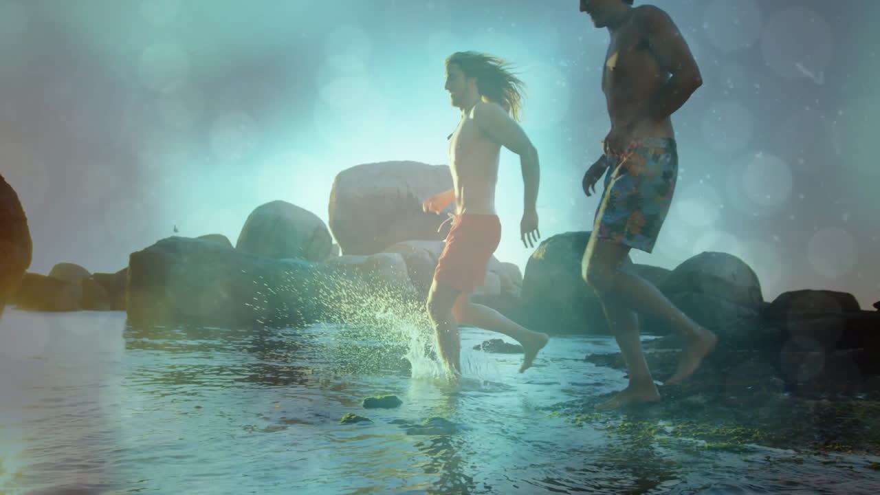 Two men stepping into rocky coastal water at sunrise, with animated health icons and wave chart