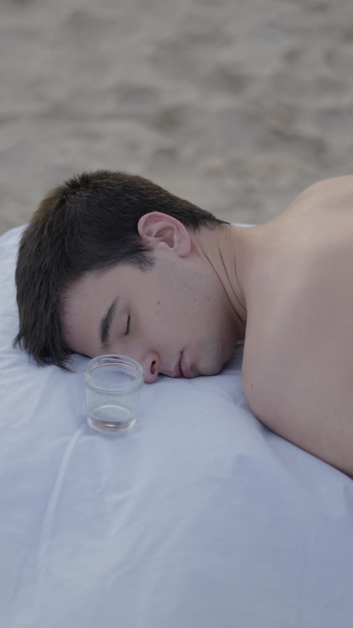 Man relaxing on a white sheet with a jar on a beach