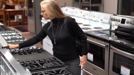 closeup of pretty mature blonde woman looking at the features and benefits of a gas stove in a kitchen appliance store